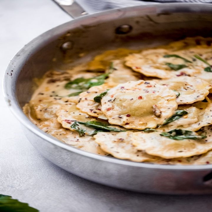 Ravioli cooking in cream sauce in a skillet.