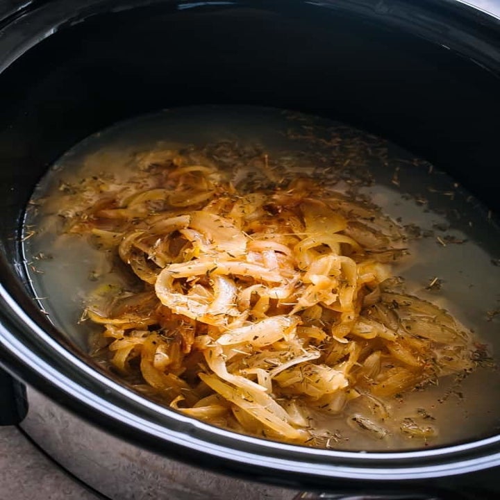 Onions cooking in broth in a slow cooker.