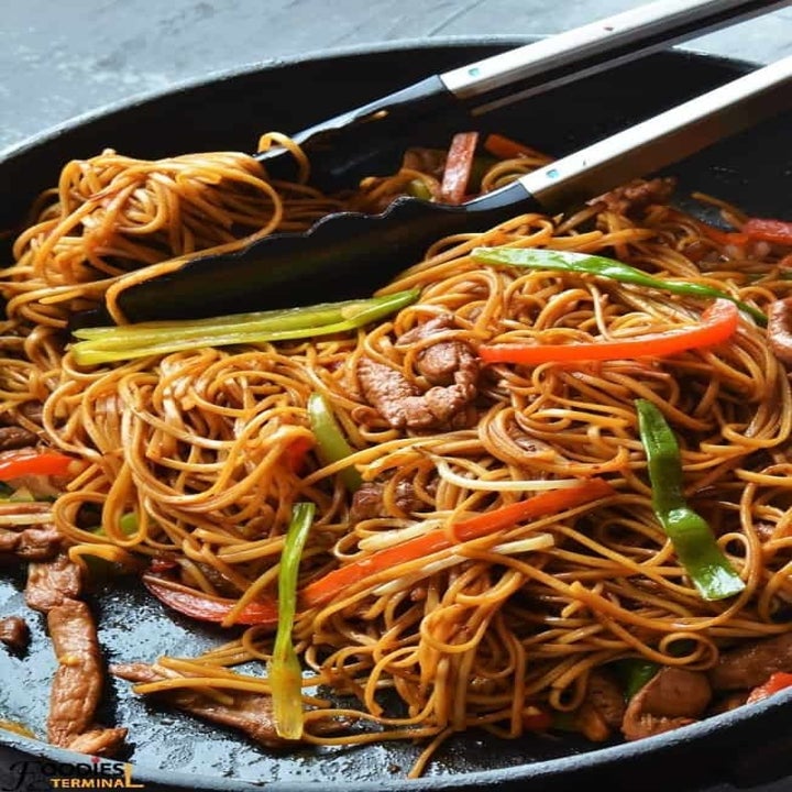 Tongs taking a scoop of chicken lo mein with veggies.
