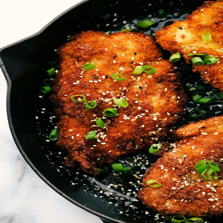 Three chicken katsu cutlets frying in a skillet.
