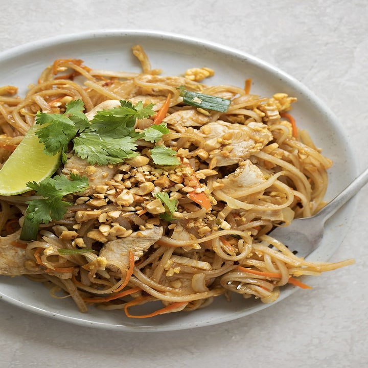 A plate of chicken pad Thai with crunchy peanuts, cilantro, and lime.