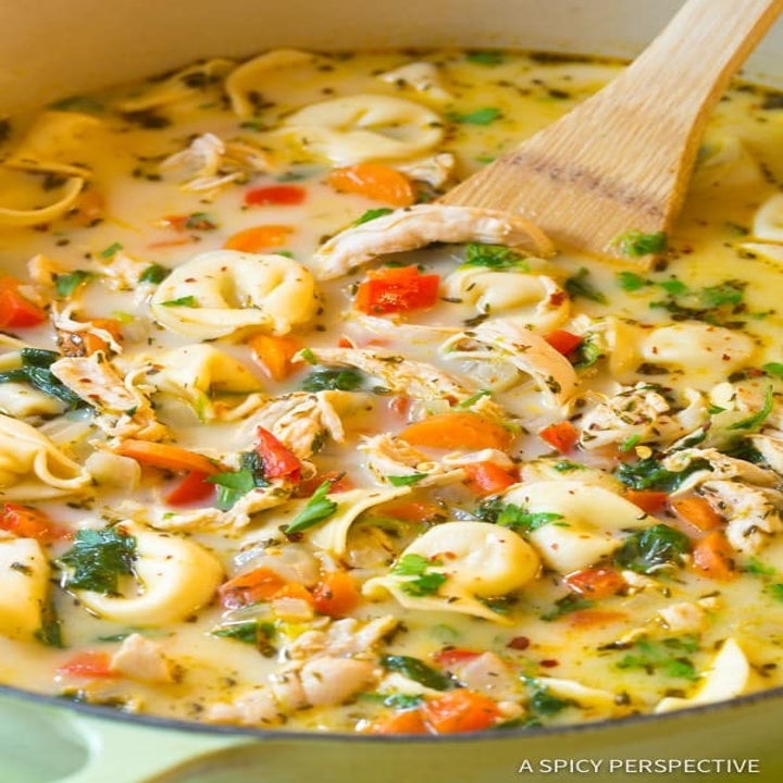 A big pot of creamy chicken soup with tortellini, carrots, and herbs.
