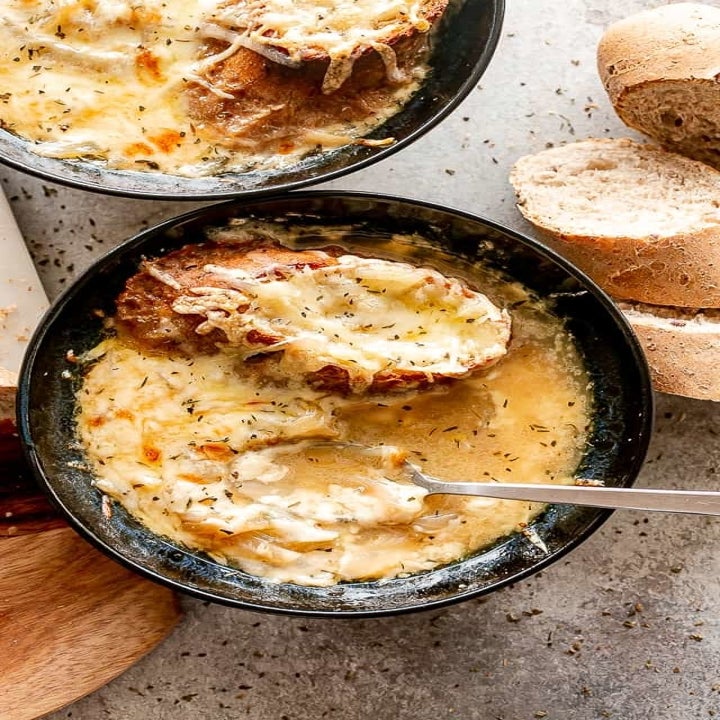 Two bowls of cheesy French onion soup with bread and melted Gruyère on top.
