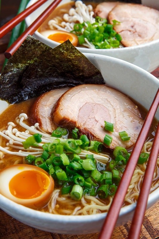 A bowl of ramen with pork belly, soft boiled eggs, enoki mushrooms, and scallions.