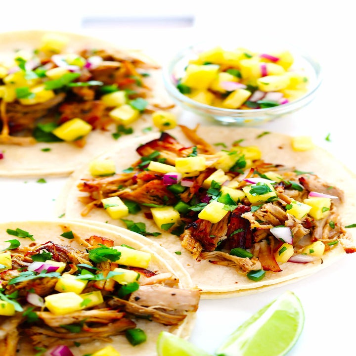 Three pork carnitas tacos topped with pineapple and herbs.