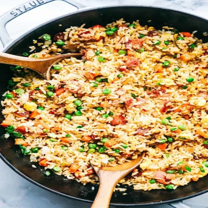 A big skillet of fried rice with bacon, peas, and carrots.