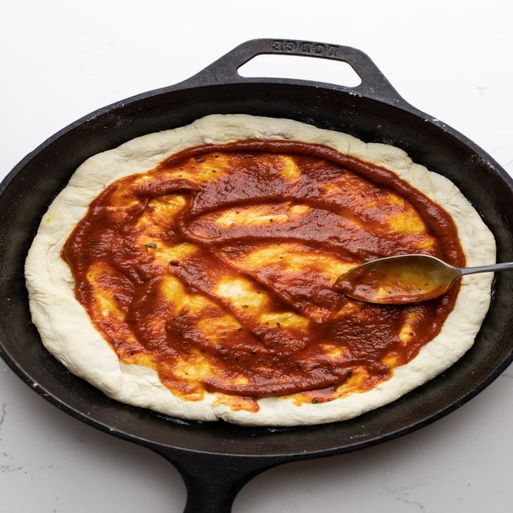 Pizza dough topped with tomato sauce in a cast iron skillet.