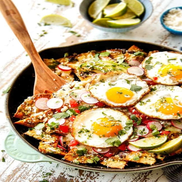 A skillet of chilaquiles with fried eggs and lots of Mexican toppings.