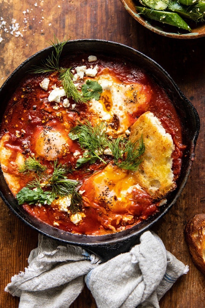 A cast iron skillet of baked eggs in tomato sauce with feta and herbs.