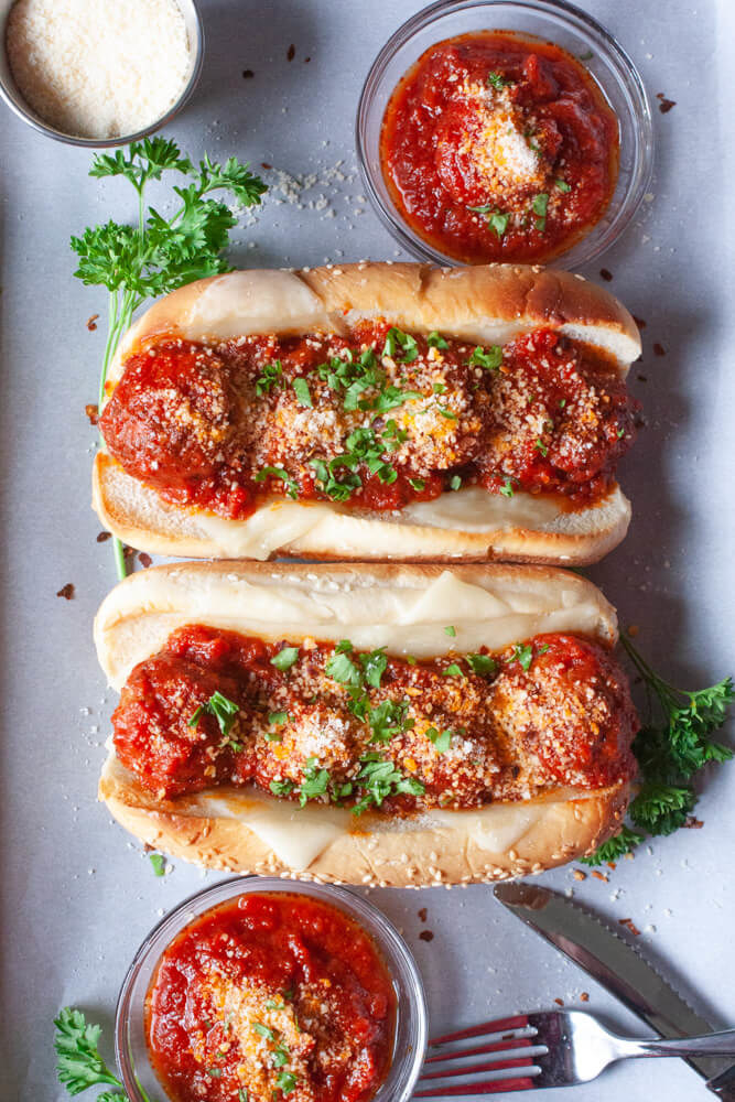 Two hotdog rolls stuffed with meatballs, tomato sauce, parmesan, and fresh herbs.