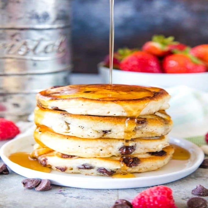 A stack of chocolate chip pancakes with a maple syrup drizzle.