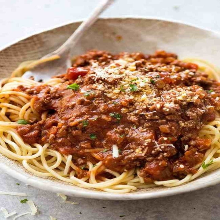 A plate of spaghetti with Bolognese sauce and grated cheese.