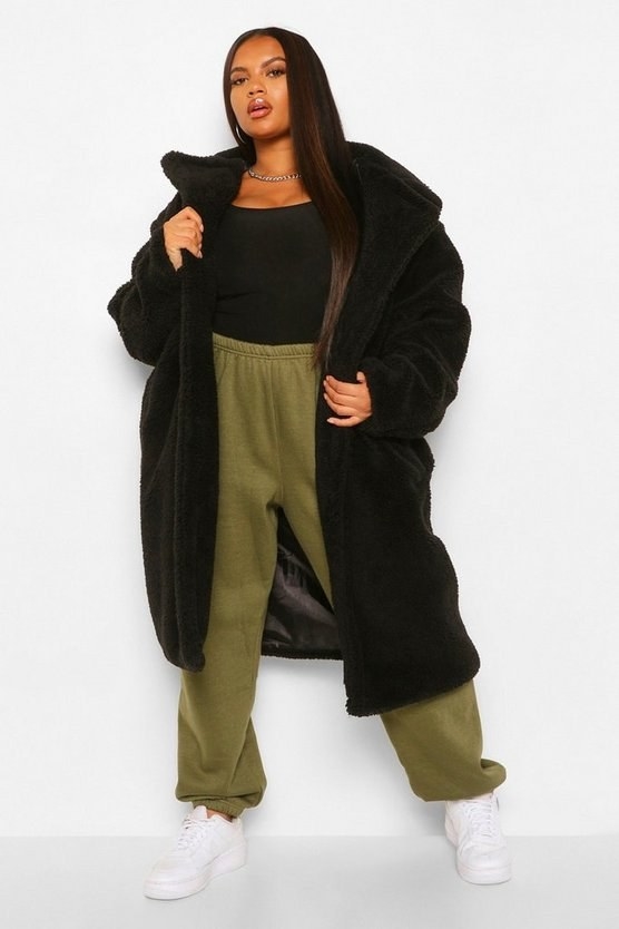 Model dressed in a full outfit with black maxi coat on