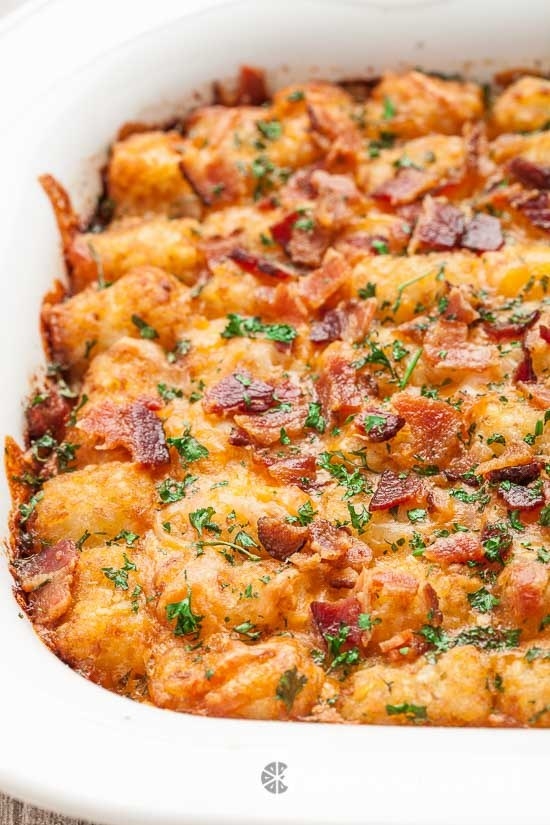 A tater tot casserole topped with bacon bits and fresh herbs.