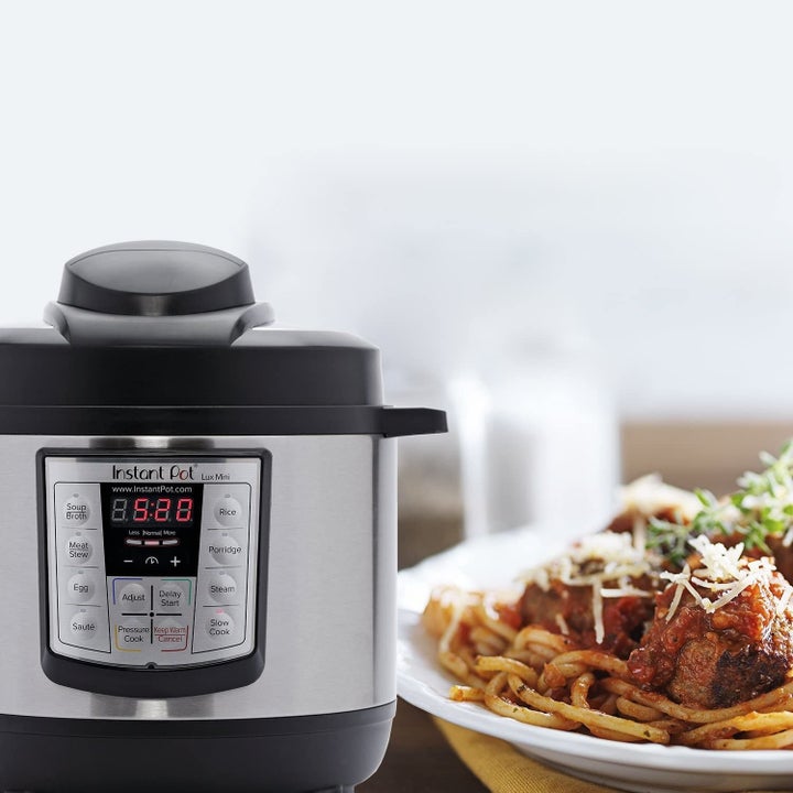 Silver and black Instant Pot next to plate filled with spaghetti and meatballs