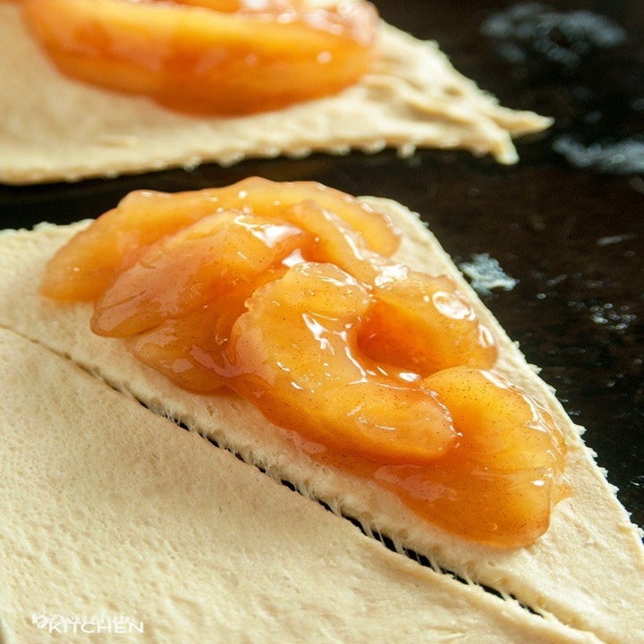 Apple pie filling being spooned into crescent dough triangles.