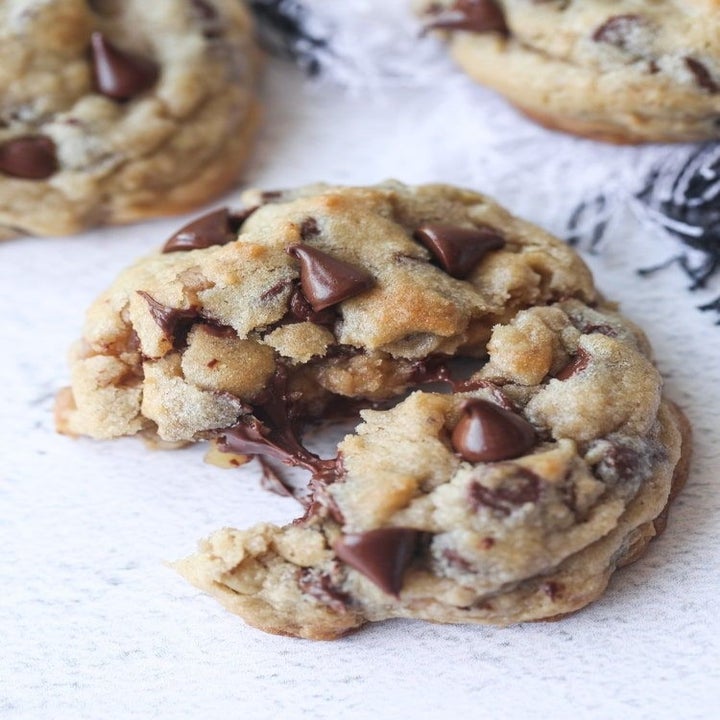 Three chocolate chip cookies on a napkin, one with a bite taken out of it.