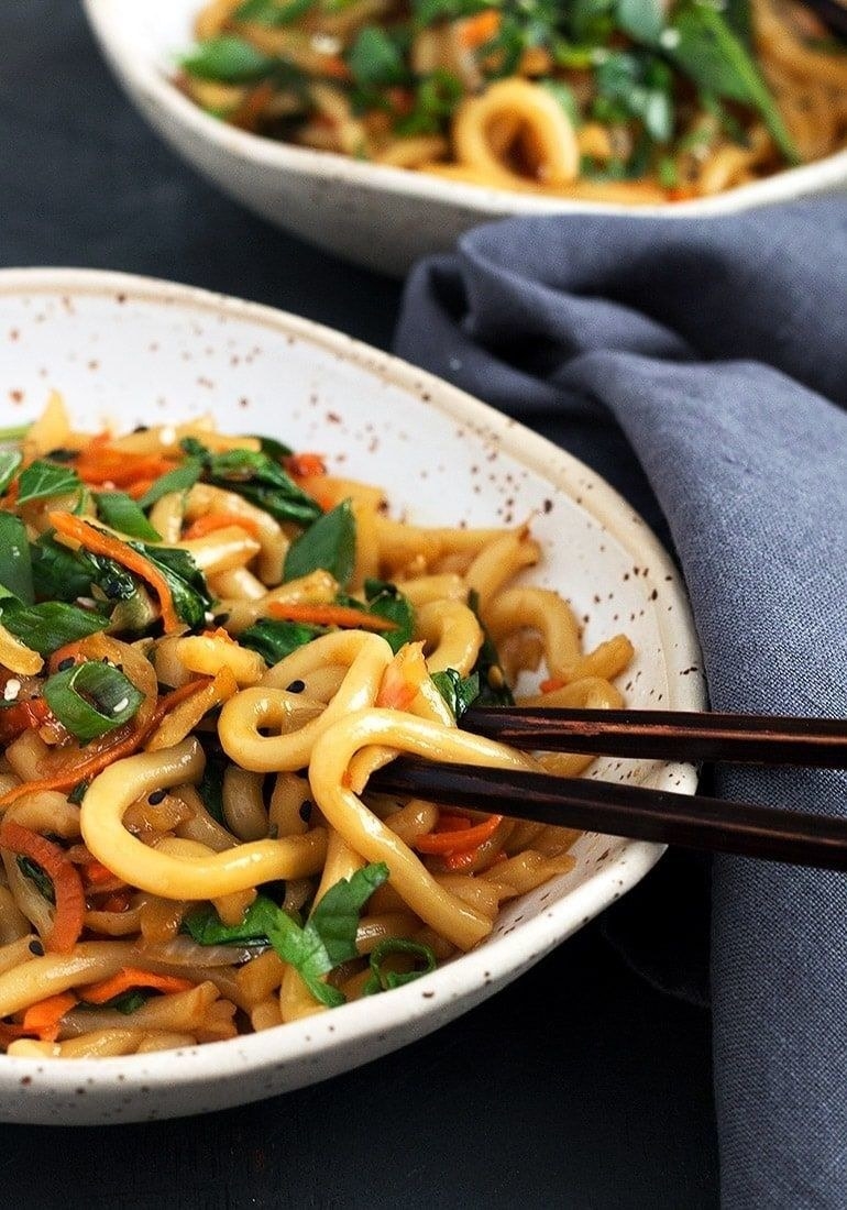 A bowl of udon noodle stir fry with carrots, scallions, and sesame seeds.