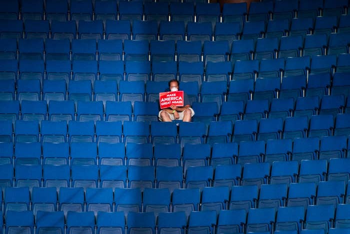Lone Trump supporter holding a sign that says, "Make America Great Again," and sitting in the stands at a rally site