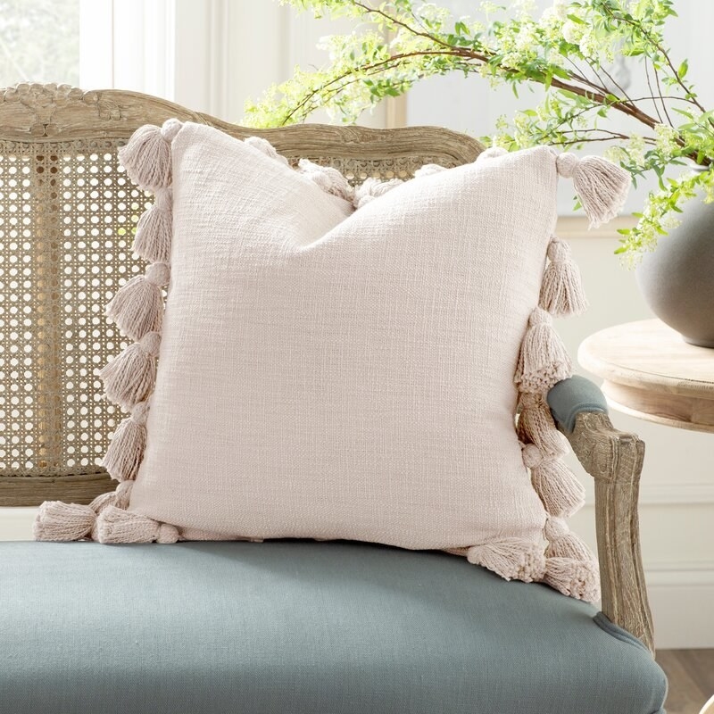 a light pink linen square through pillow with tassels all around the edges