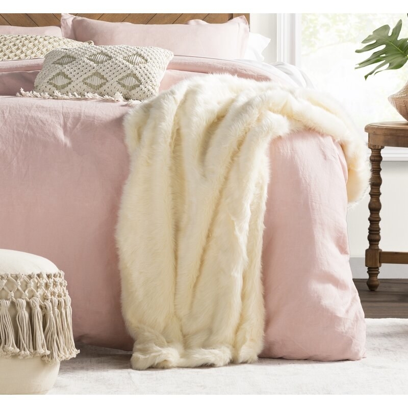 an offwhite faux mink throw blanket on the edge of a light pink bed