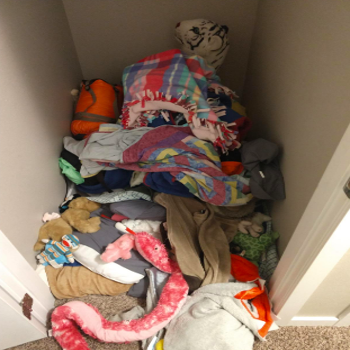 Closet filled with clothes and blankets on floor, spilling out into room 