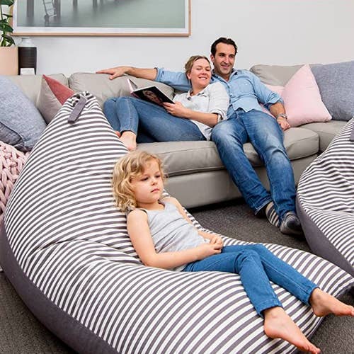 Parents on sofa with young child sitting on large stuffed chair on floor 