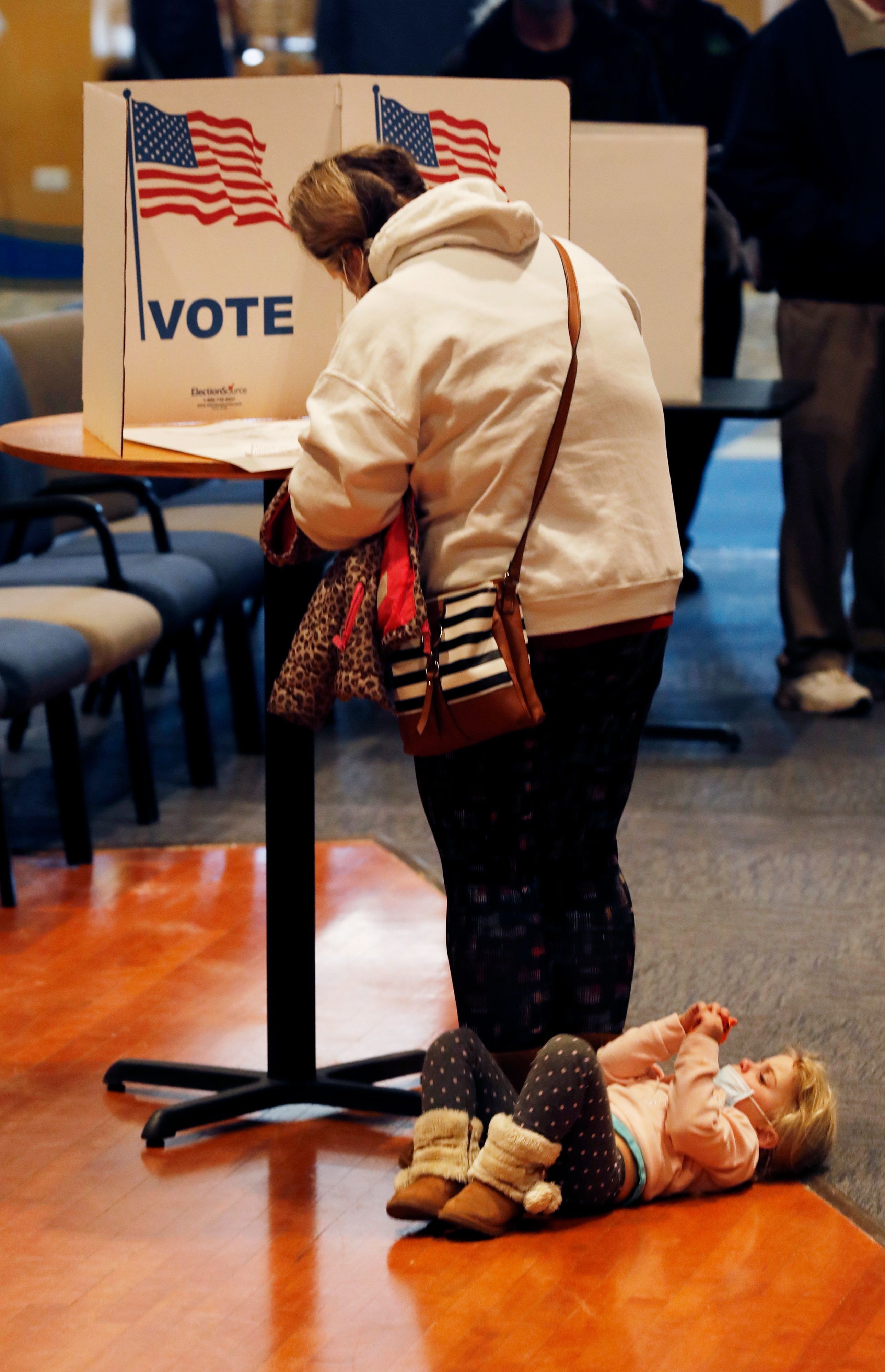 child lies at parents feet while they vote