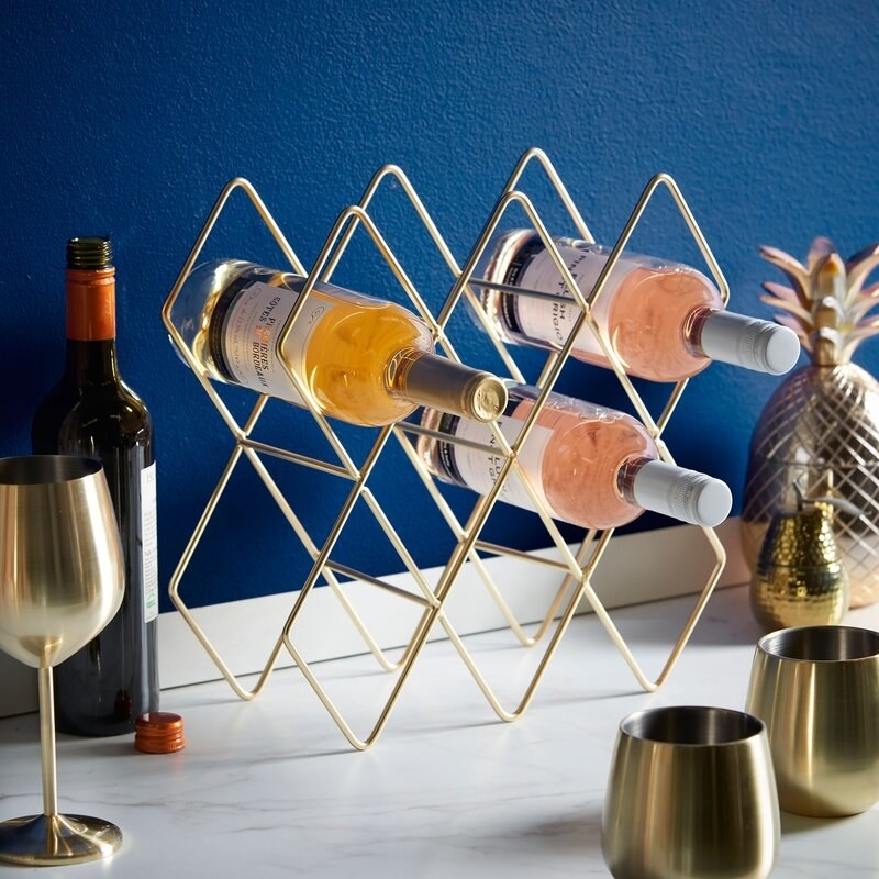a gold wire wine rack holding three bottles of wine on a counter