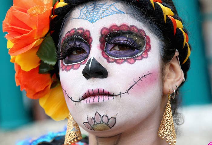 A woman with her face painted as a skull and her braided hair adorned with flowers for Día de los Muertos 