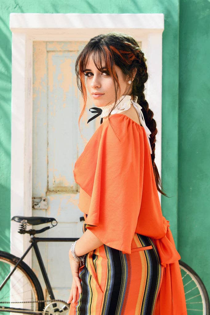 Camila with her hair in two braids standing in front of a bicycle that&#x27;s leaning against a door