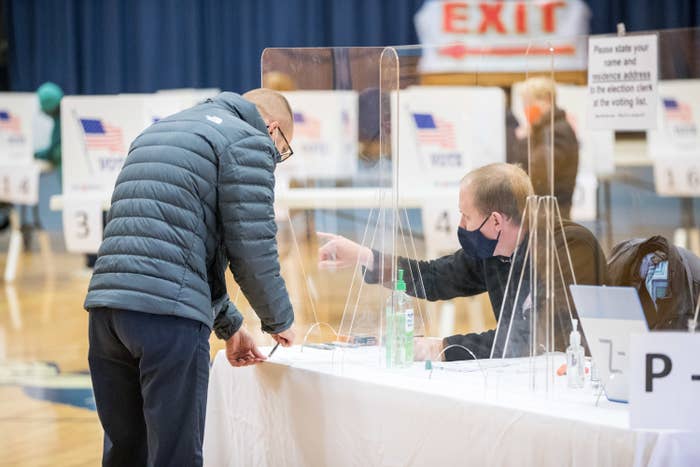 Man speaking to a poll worker behind a plastic barrier