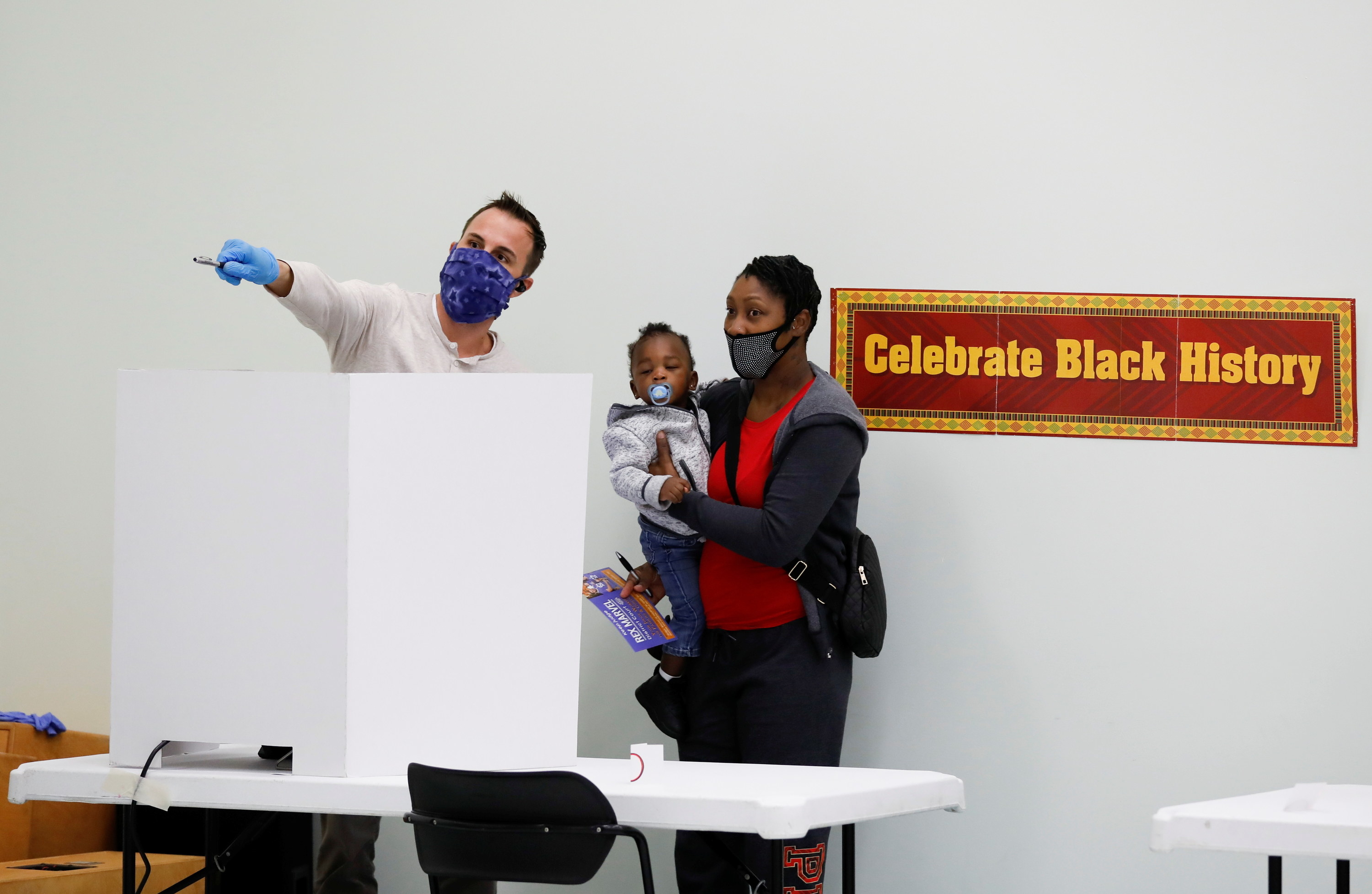 Man pointing and mother holding her baby at a polling place. 