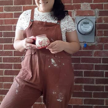 A reviewer wearing brown overalls splattered with clay spots layered over a T-shirt
