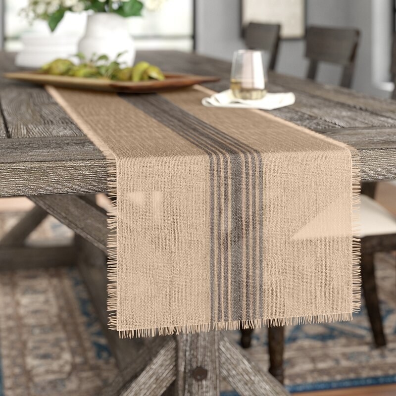 a brown sheer table runner with black stripes running down the middle on a wooden table