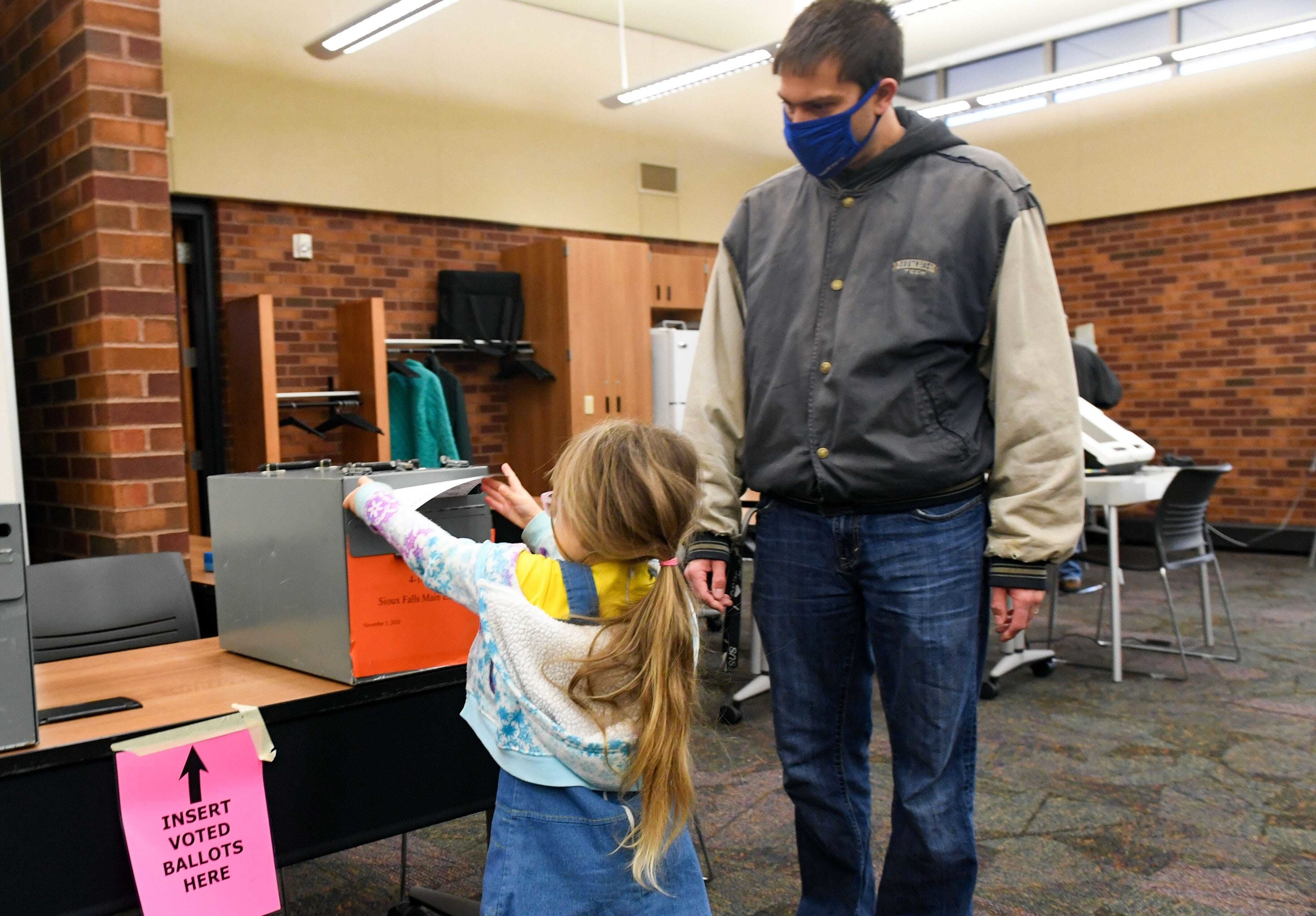 Young girl with ponytail helping her father vote. 