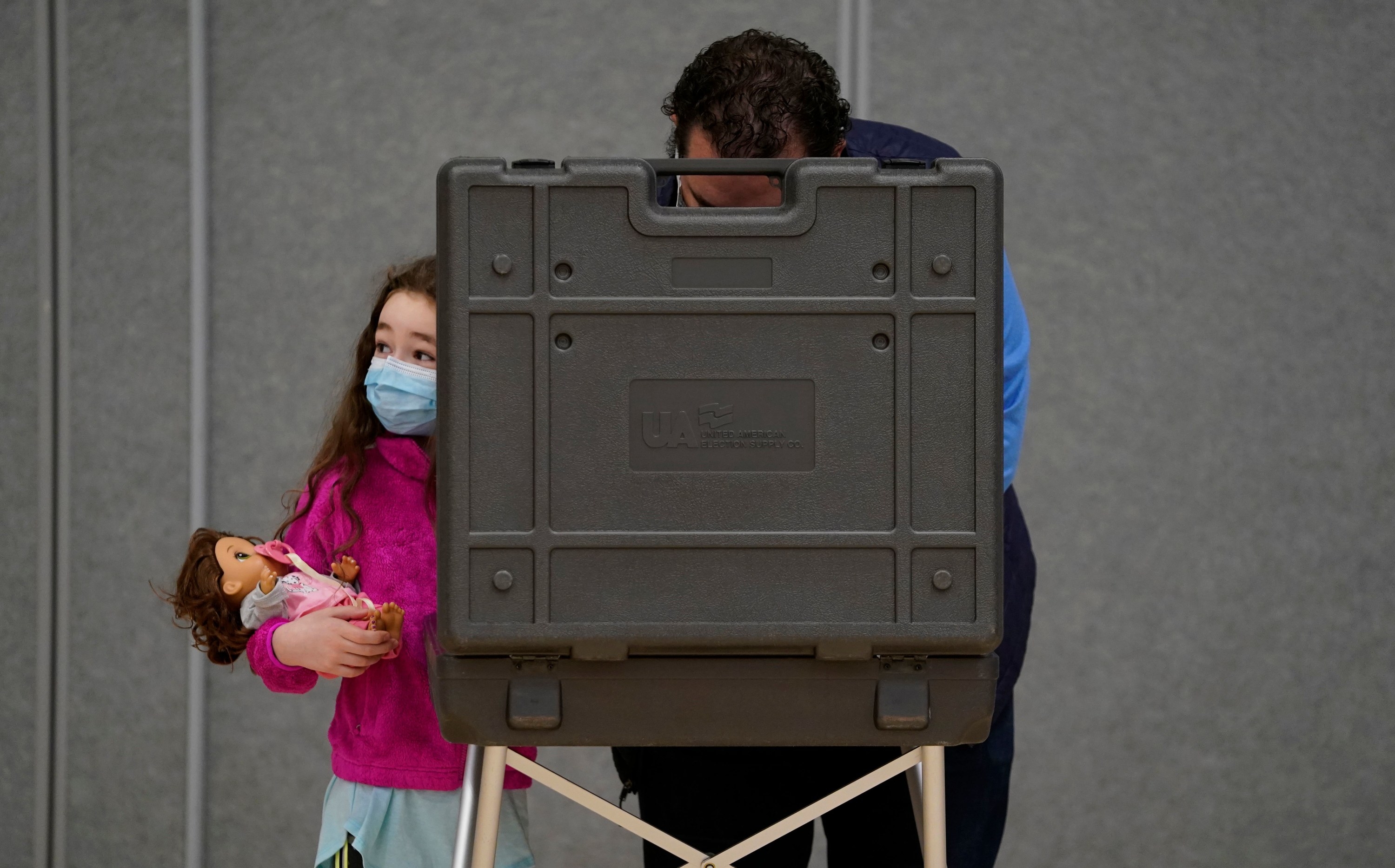 Girl with doll waiting for her father to vote. 
