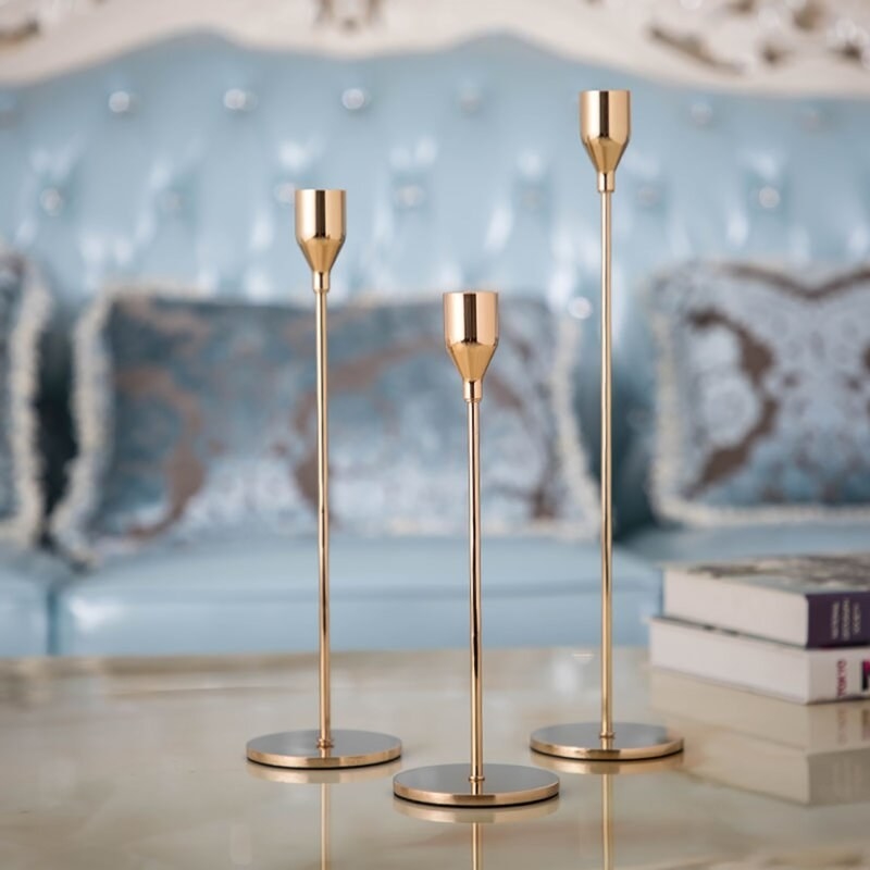 three long mid-century modern golden candlesticks of varying lengths on a coffee table