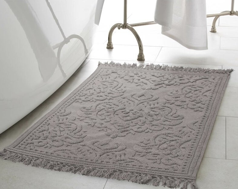 a grey bath rug with a woven design and tassels on either end of the rug