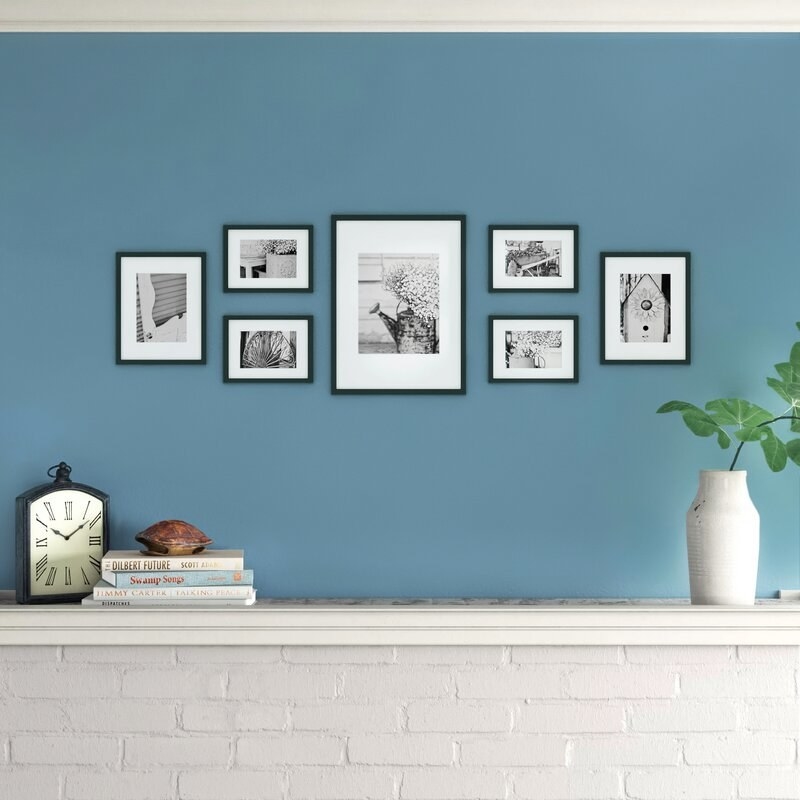 7 black picture frames of varying sizes on a wall above a mantle