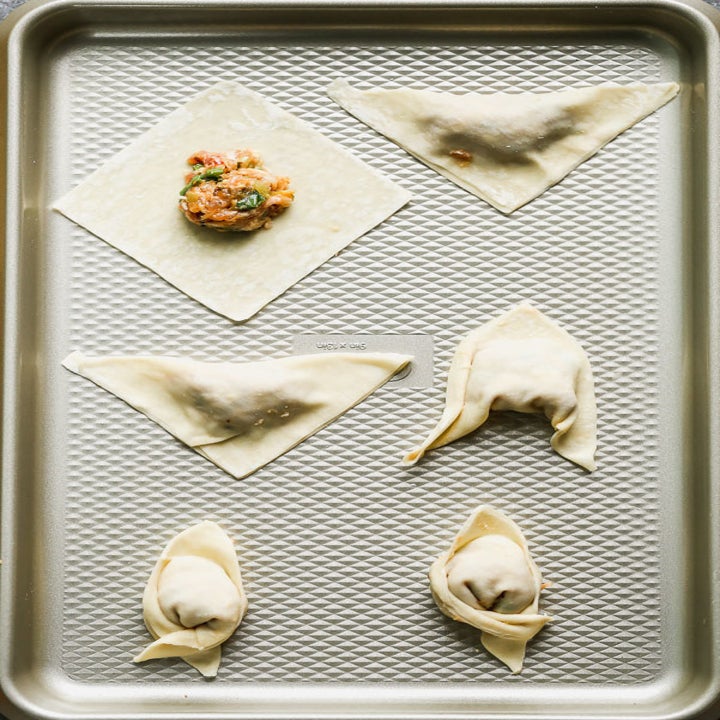 Wontons filled with pork on a baking sheet.
