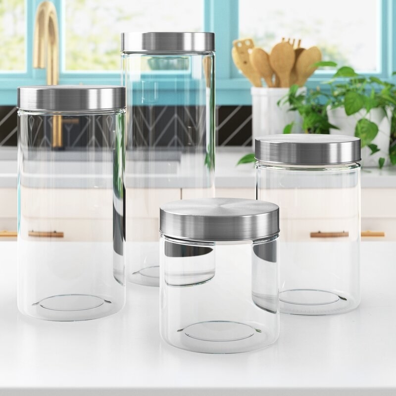 four glass cylindrical canisters with stainless steel screw-on tops on a kitchen counter