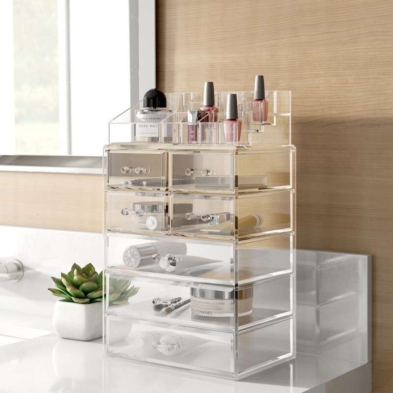 an acrylic cosmetic organizer with three large drawers, four small drawers, and a tiered shelf on top for smaller cosmetic items