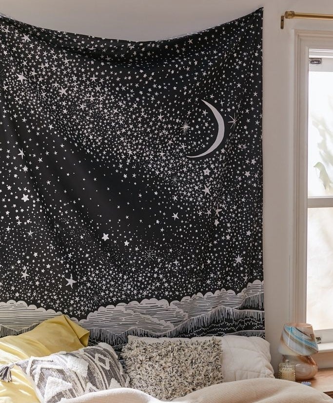 black tapestry with a white crescent moon and several white stars hanging above a bed 