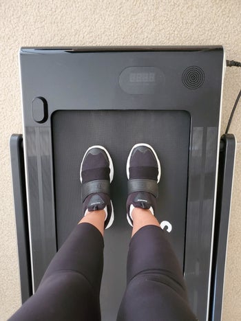 pic of reviewer placing feet on black treadmill with the riser down