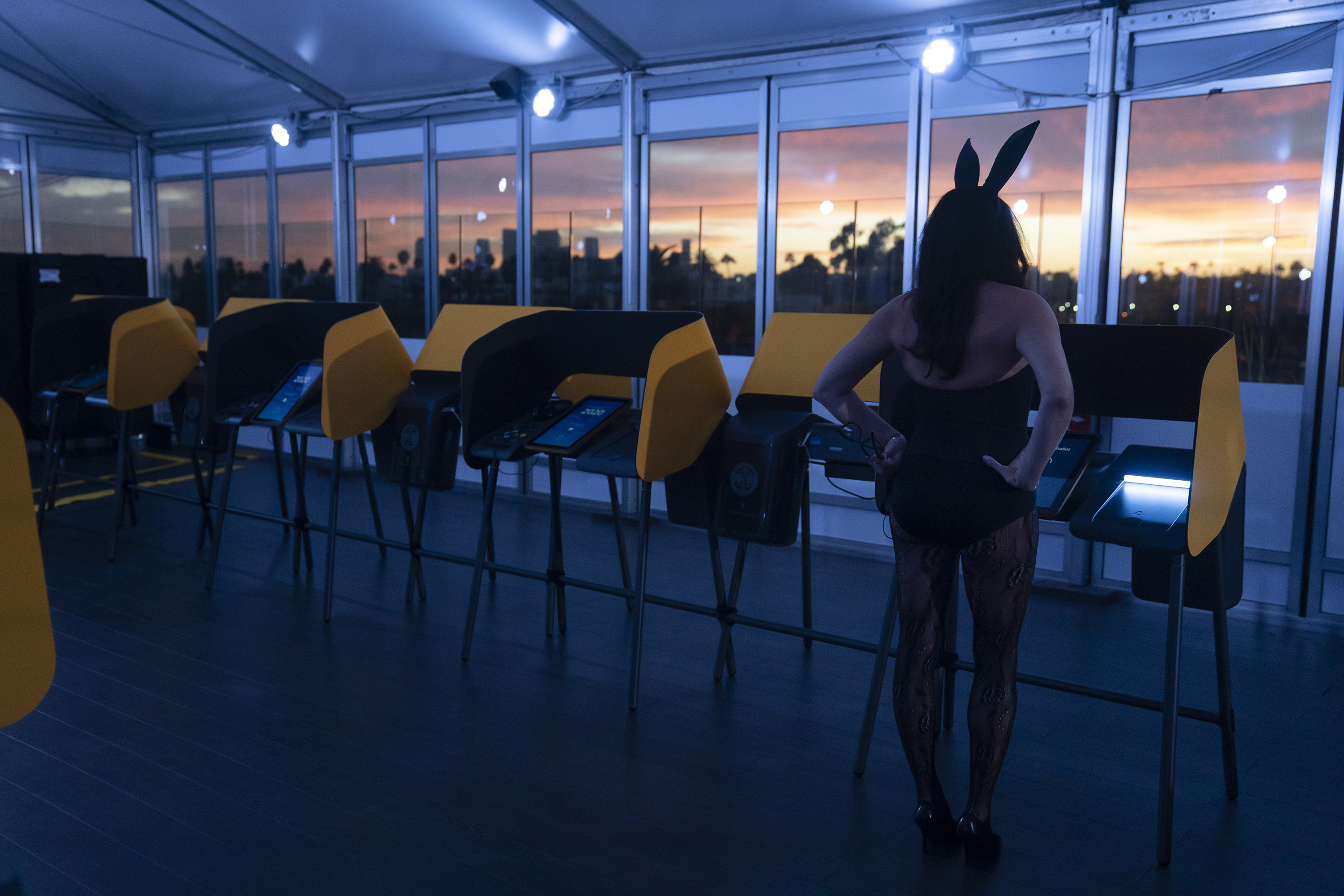 Woman in a Playboy Bunny costume at a voting booth on an enclosed rooftop. 