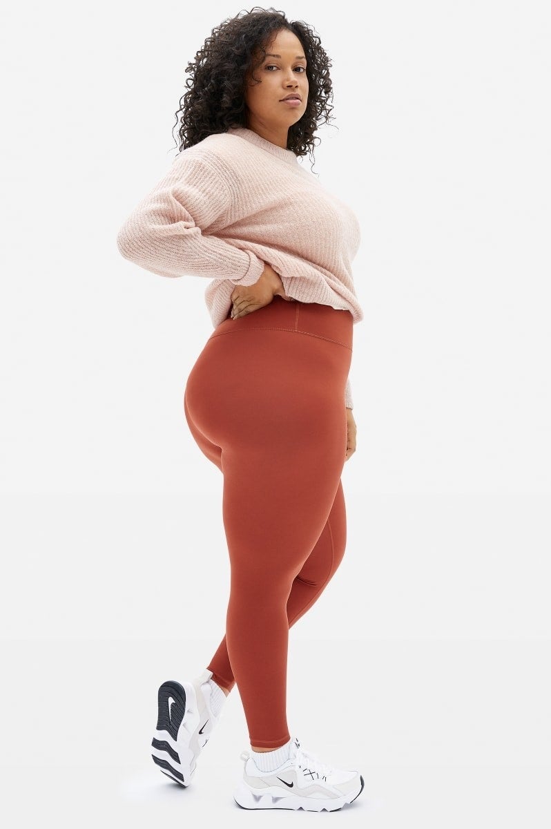 Model wears high-rise red leggings with a light pink sweater and white sneakers
