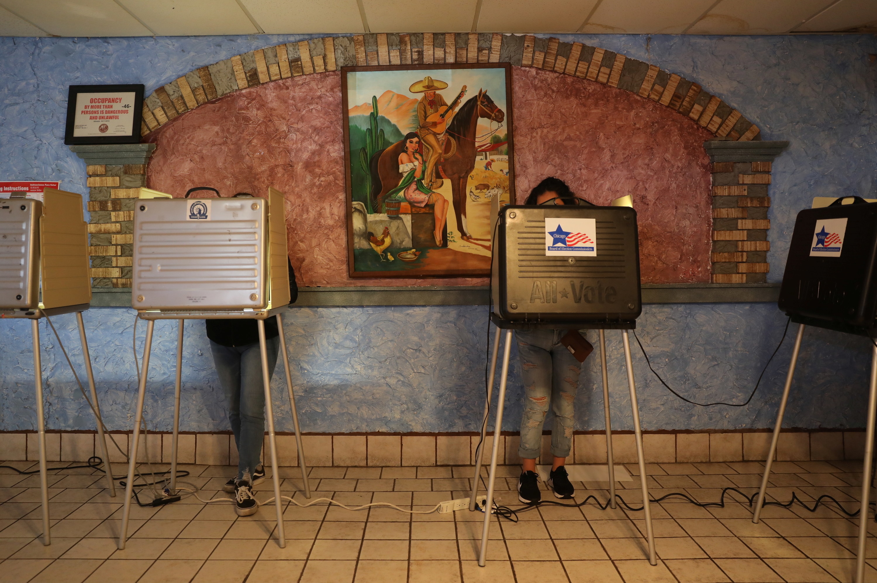 Two people at ballot stations under a mural in a Mexican restaurant. 