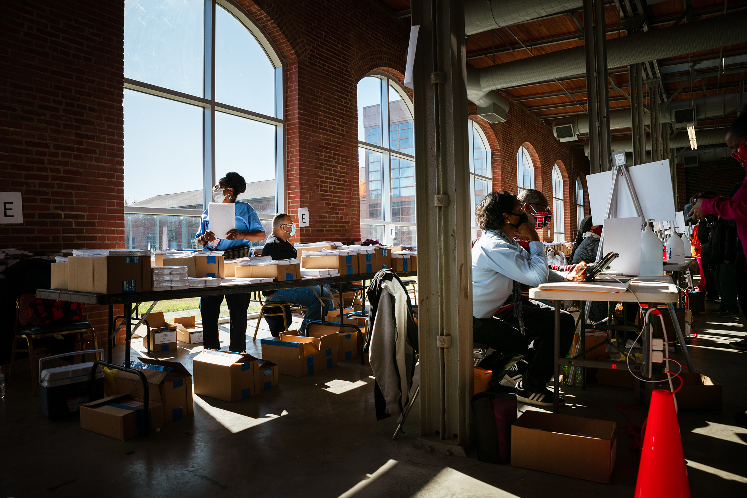 People at desks with polling centers in a well-lit building. 