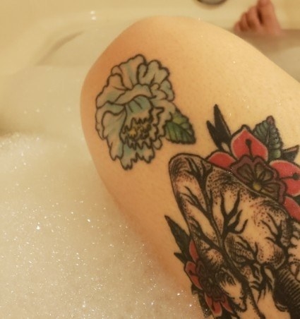 A tattoo of a blue flower with a single leaf on someone&#x27;s knee